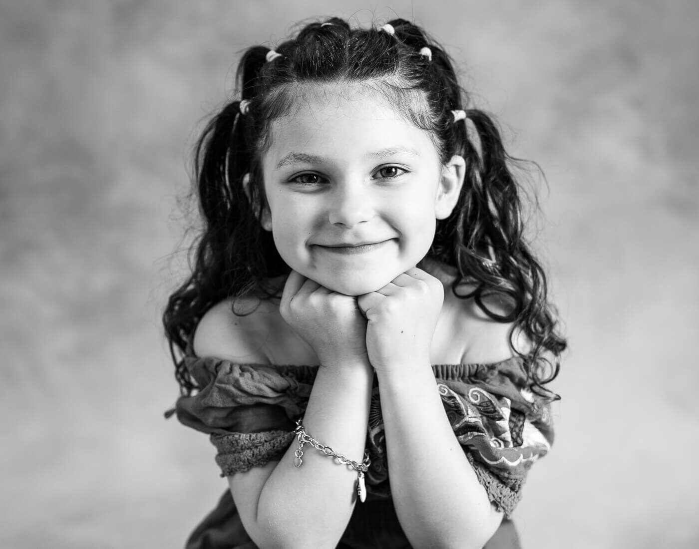 A child poses with her hands on her chin.