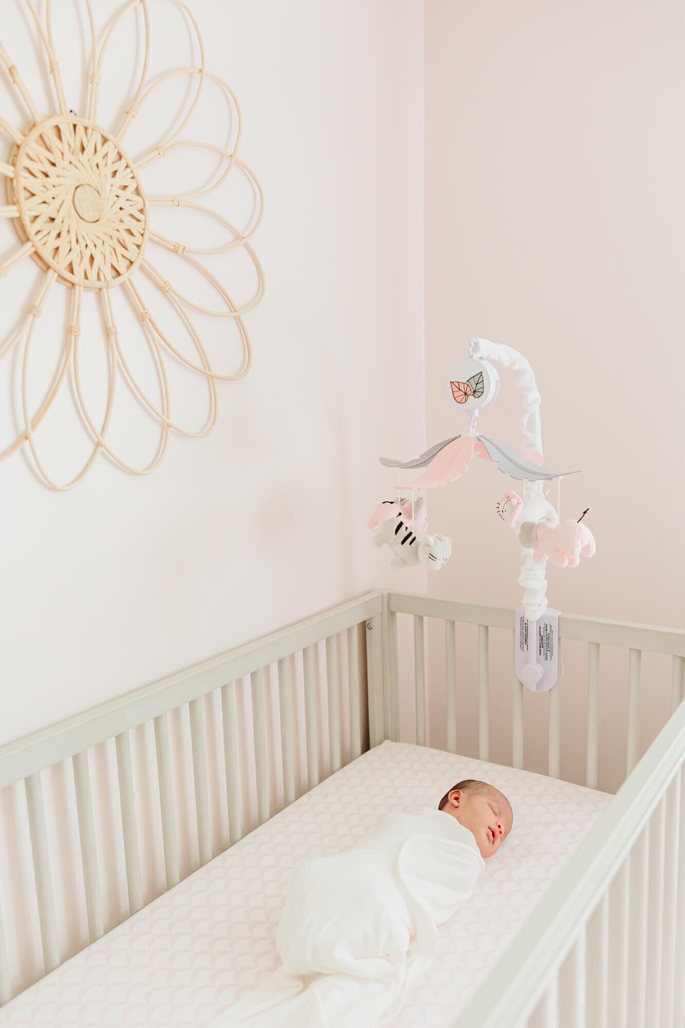 Newborn sleeping in her crib underneath a grey and pink mobile