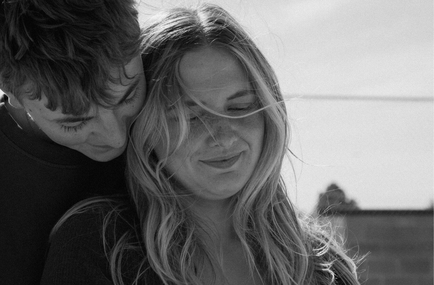 Black and white photo of a couple looking down towards the ground and smiling.