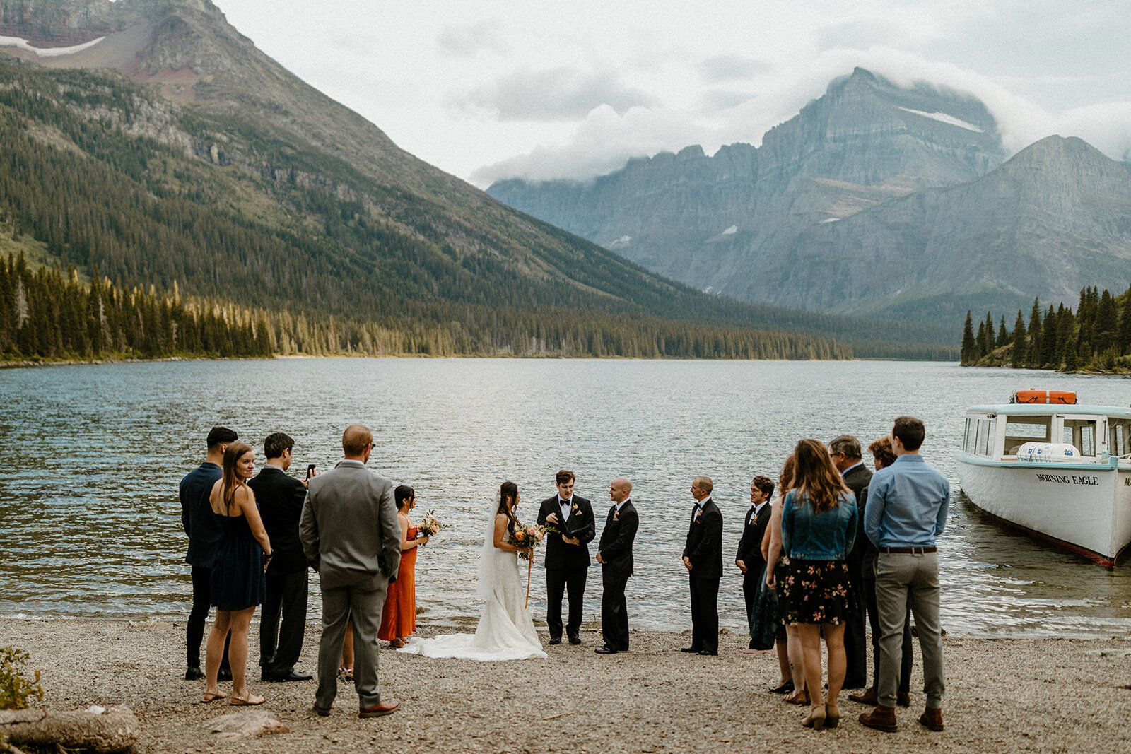 Intimate lakeside wedding ceremony in Glacier National Park, with the couple exchanging vows on the shore surrounded by family and mountain views.