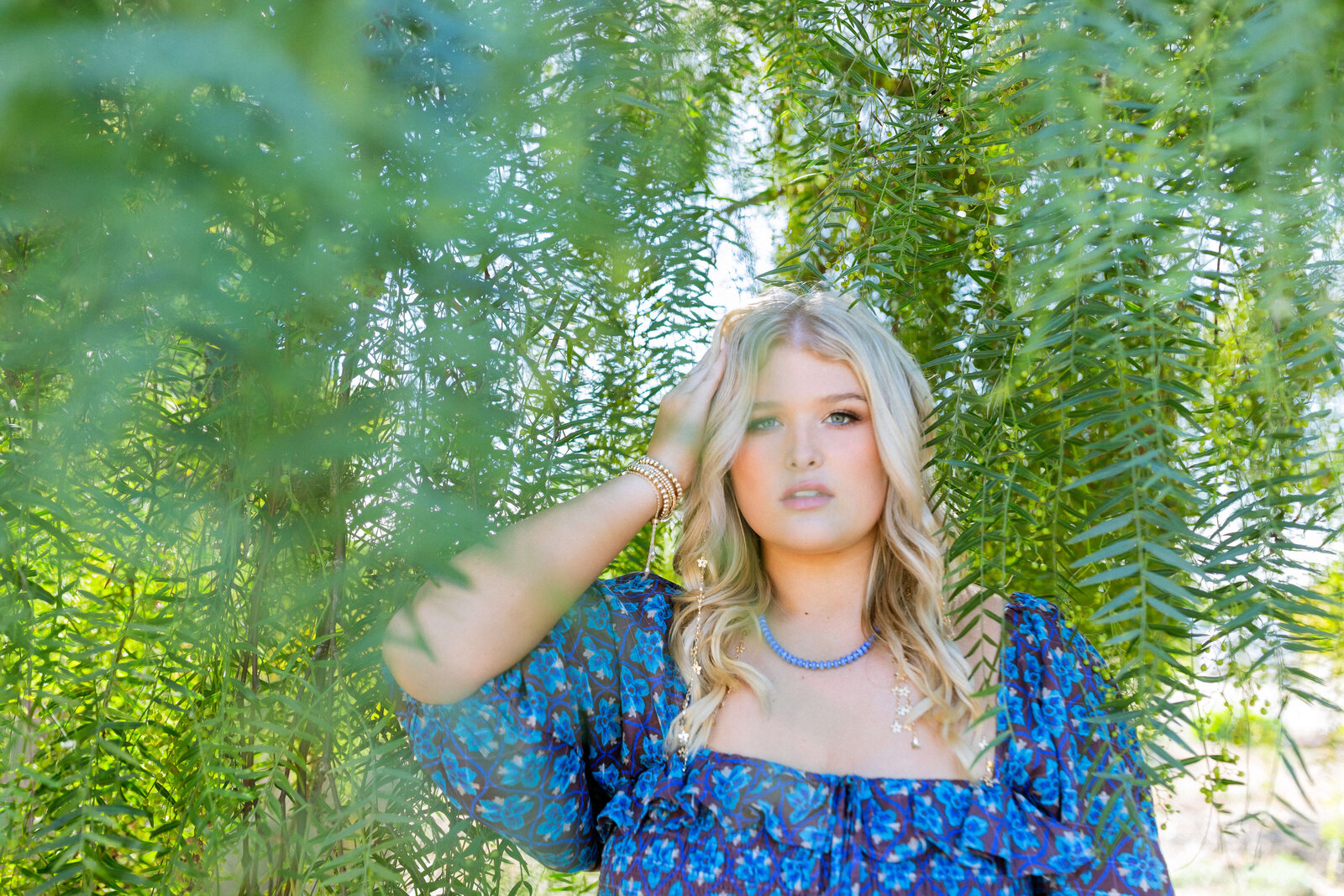 blonde girl wearing blue dress and posing under a tree