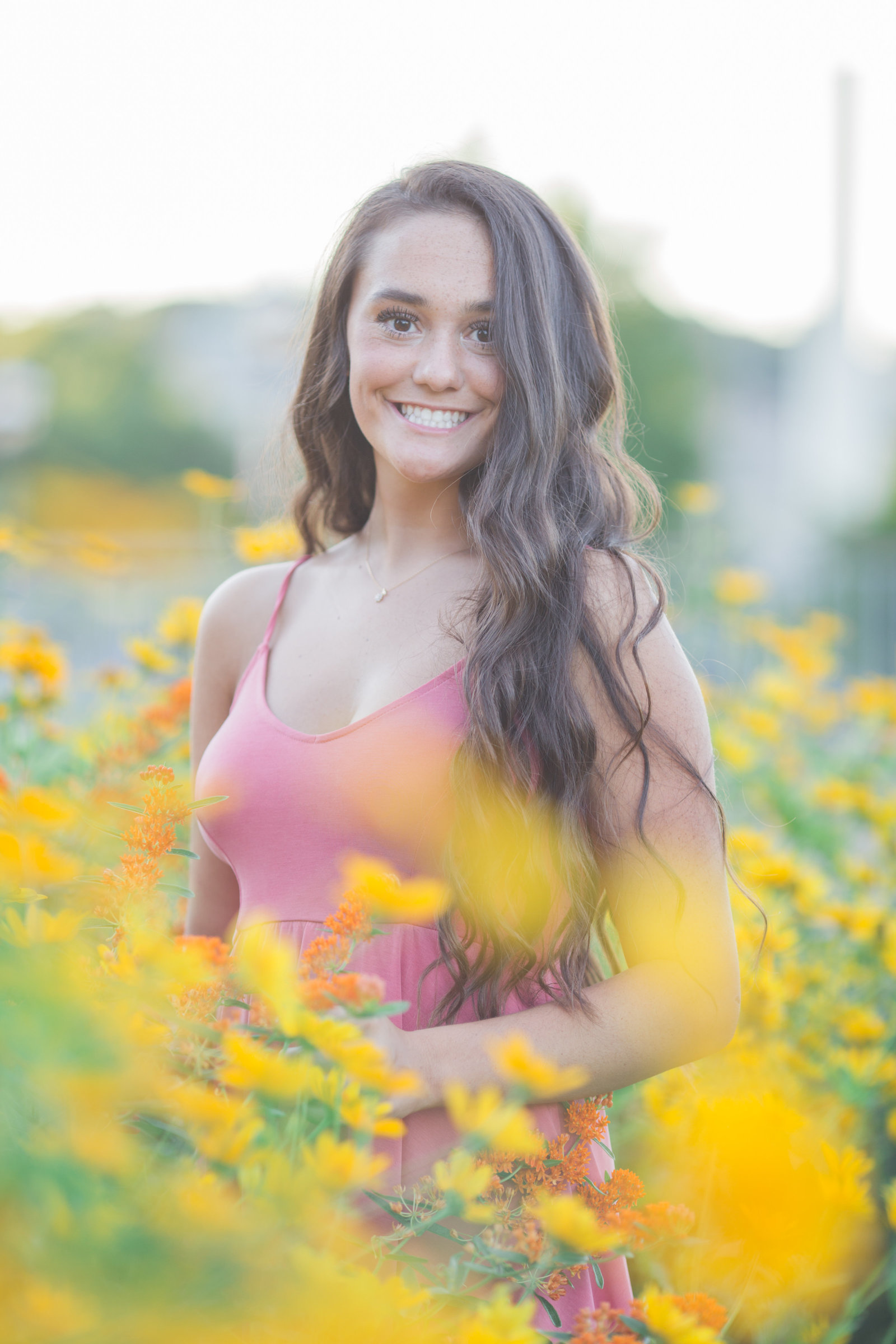 senior girl in pink dress stands amongst yellow flowers at phipps conservatory in oakland