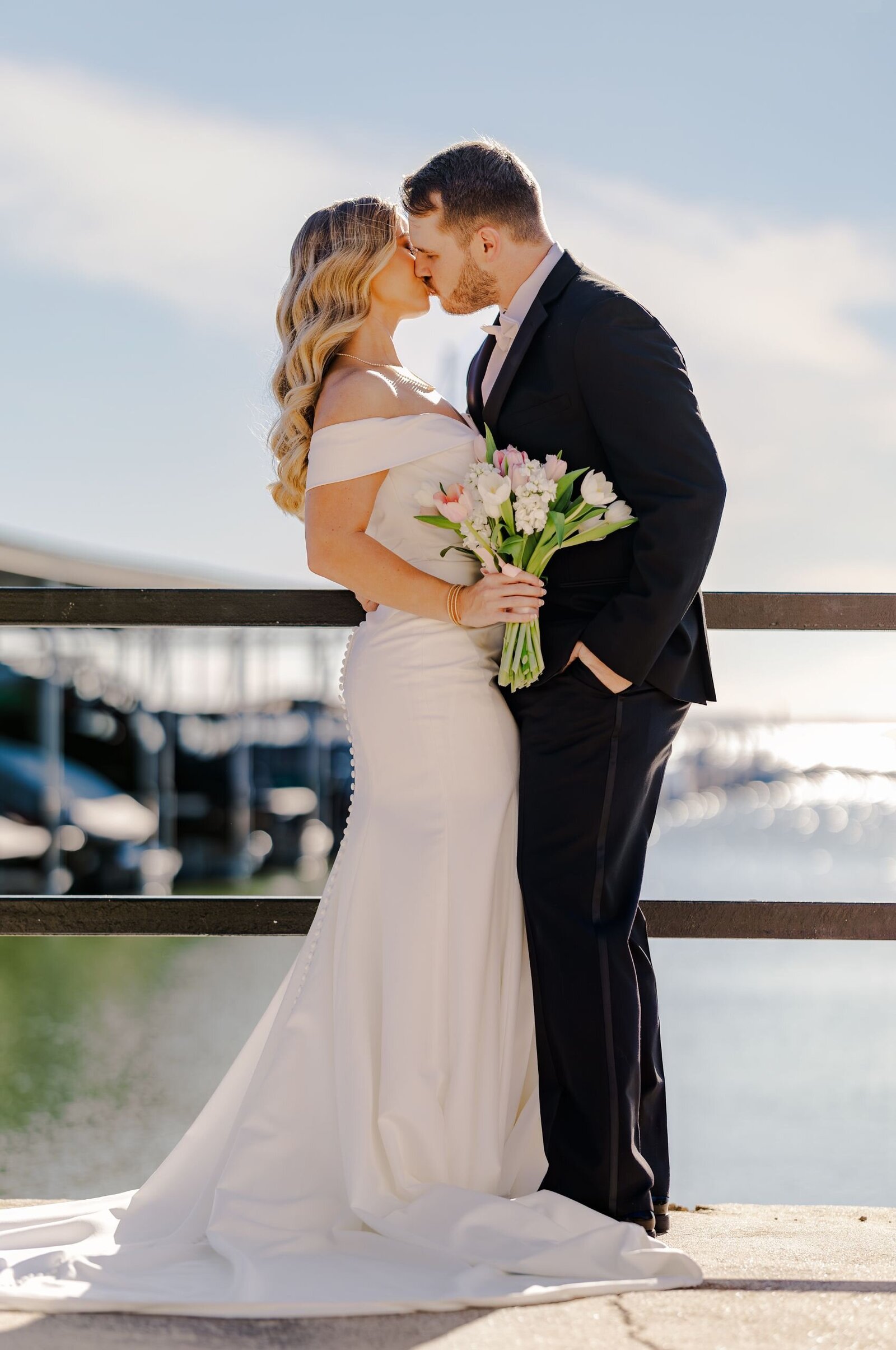 A groom leans over to kiss his bride in front of the lake where they held their wedding reception.