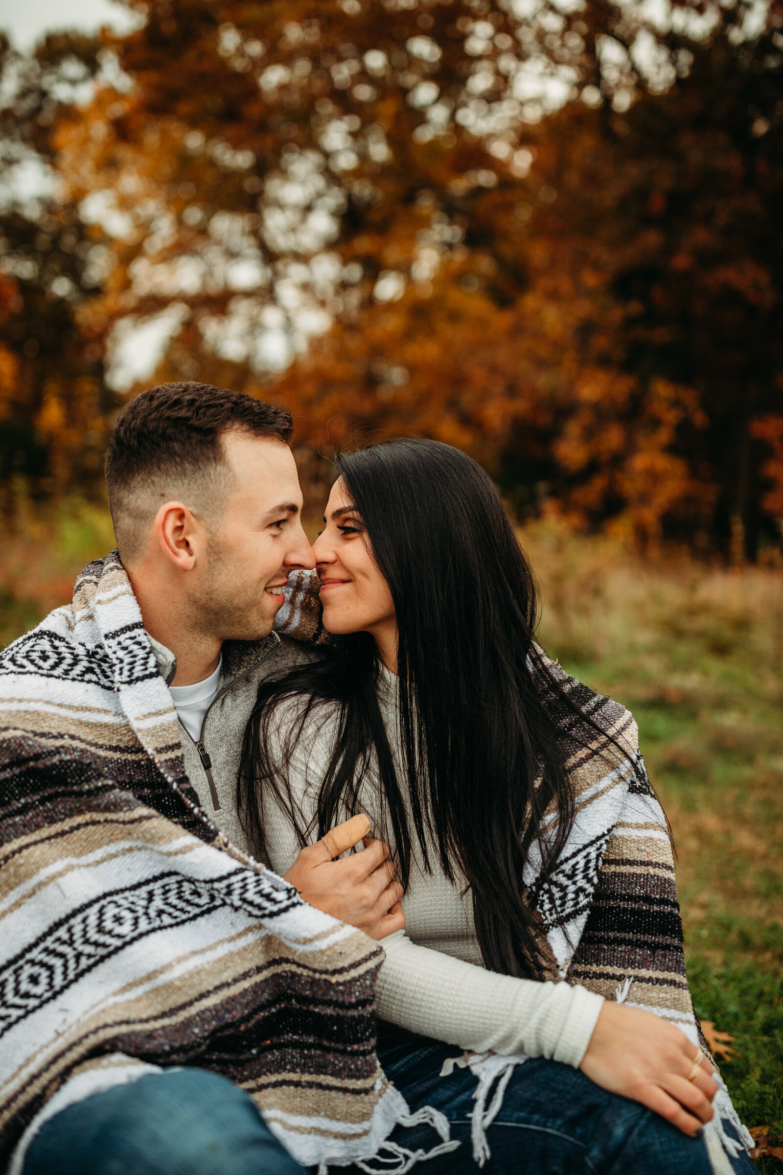 couple wrapped in blanket sits face to face during autumn photo shoot