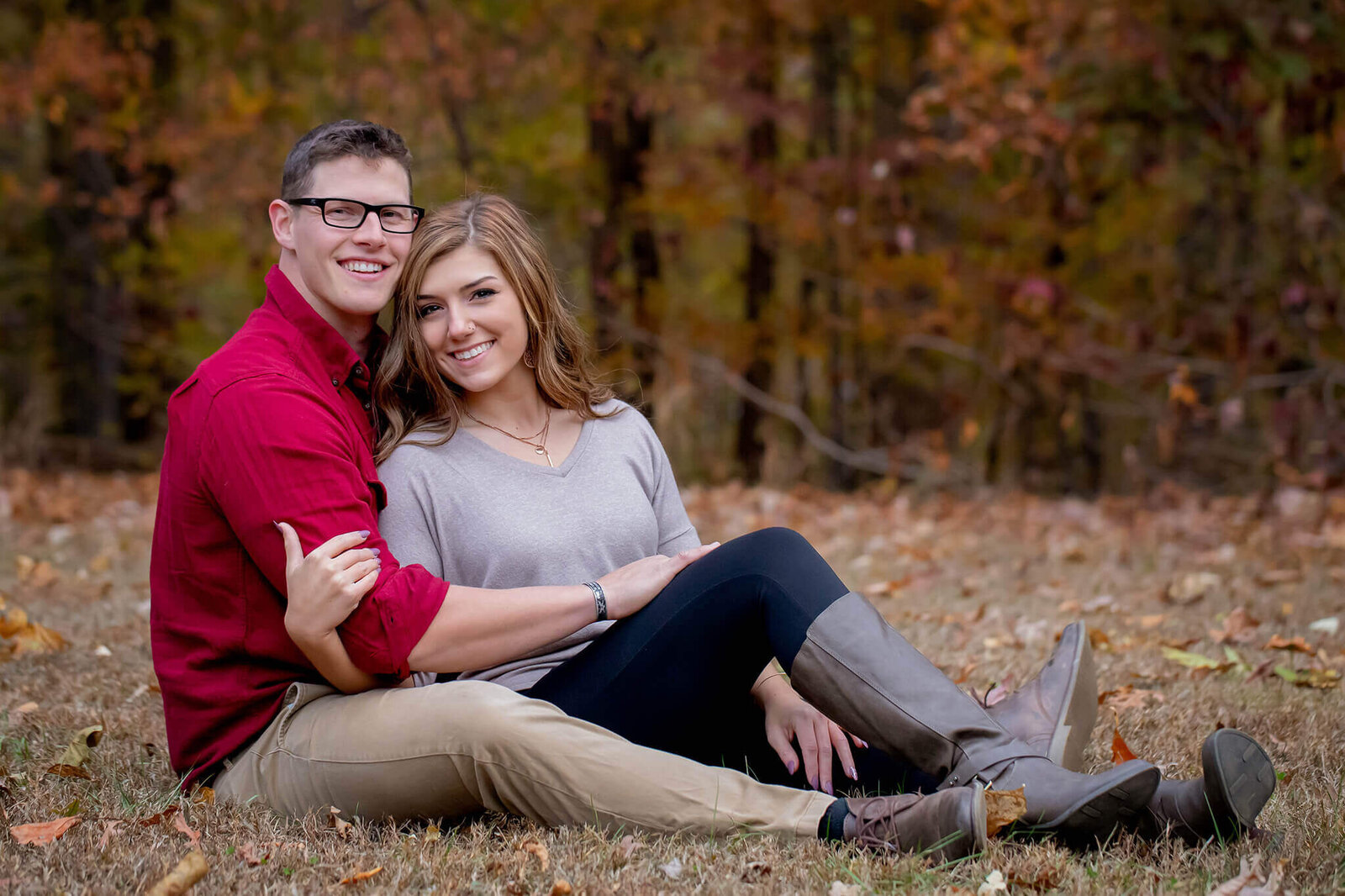 A couple sitting on the grass together among the fall foliage.