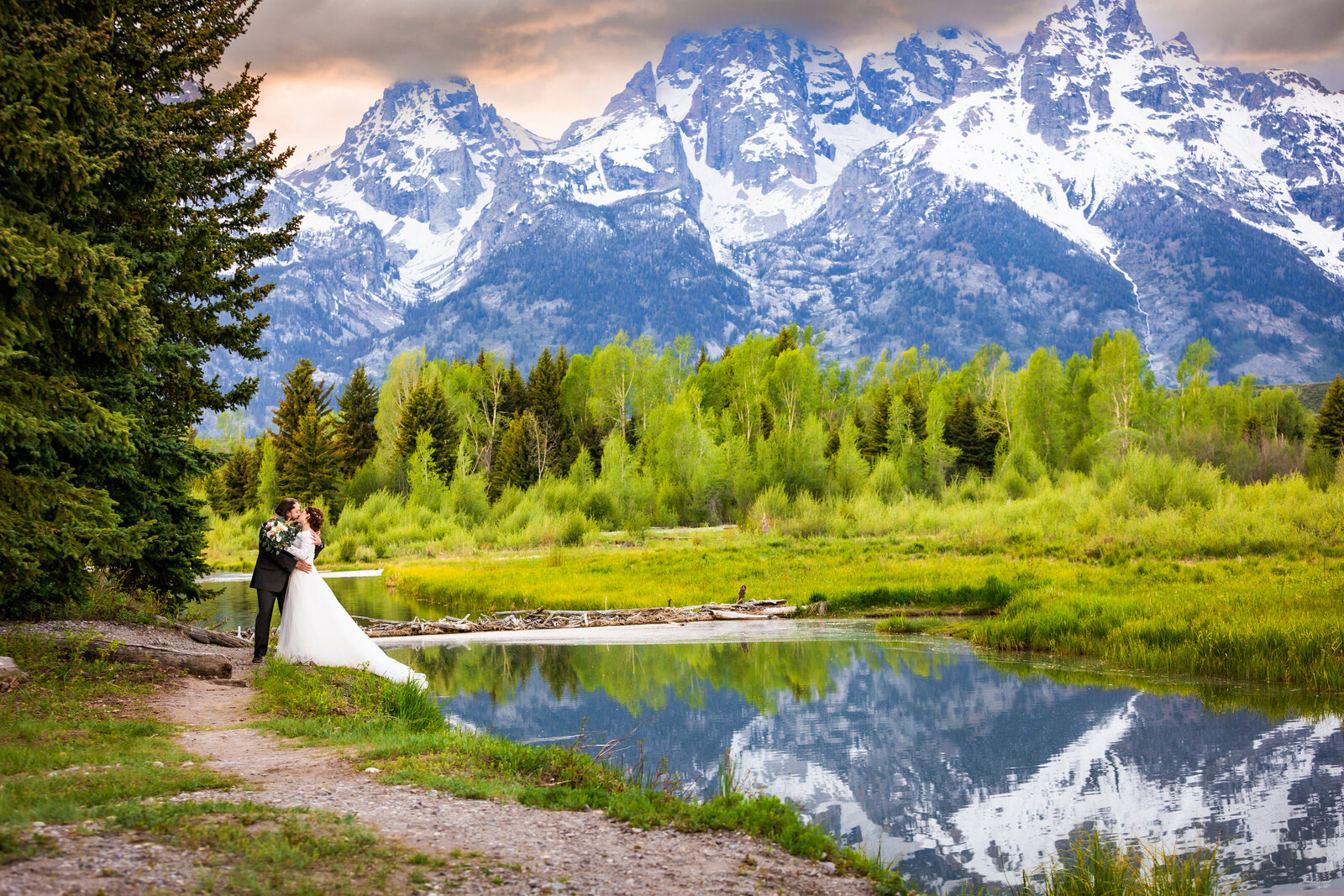 summer sunset jackson hole elopement with bright and vibrant colors. grand tetons are blue, sky is orange, foliage is green, and frame the kissing couple perfectly.
