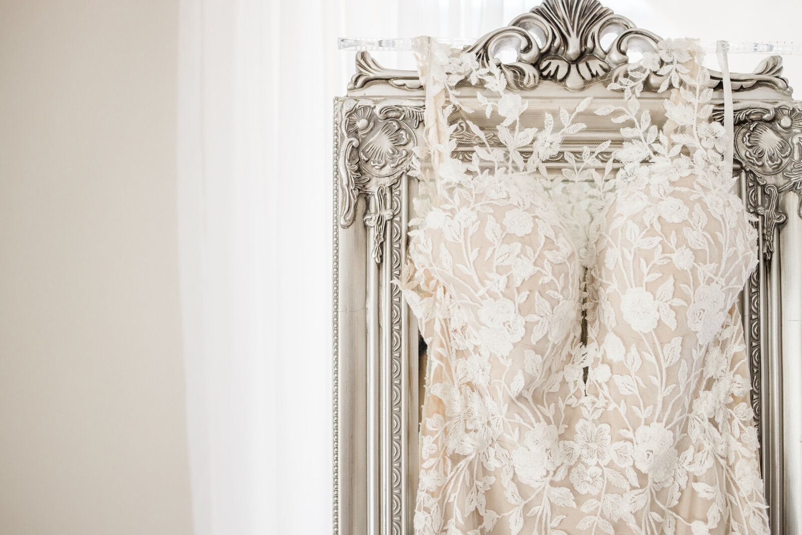 bridal dress hanging from a very fancy silver mirror