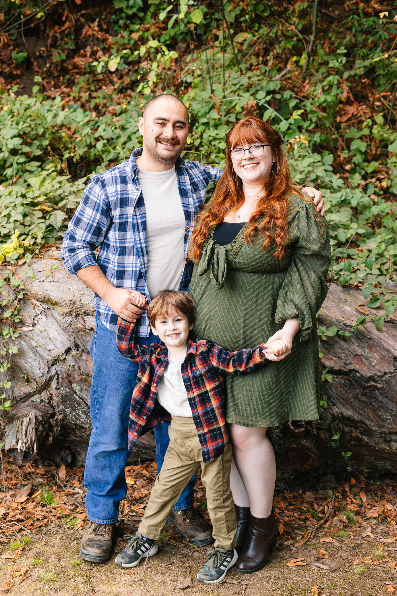 A family of 3 poses for photos in a forest in Santa Cruz, Ca.