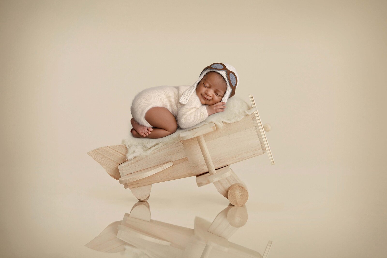 Baby sleeping on wooden airplane prop with a smile. Newborn Photography session photographed at Jenni Nikki's photo studio in Marietta, GA.