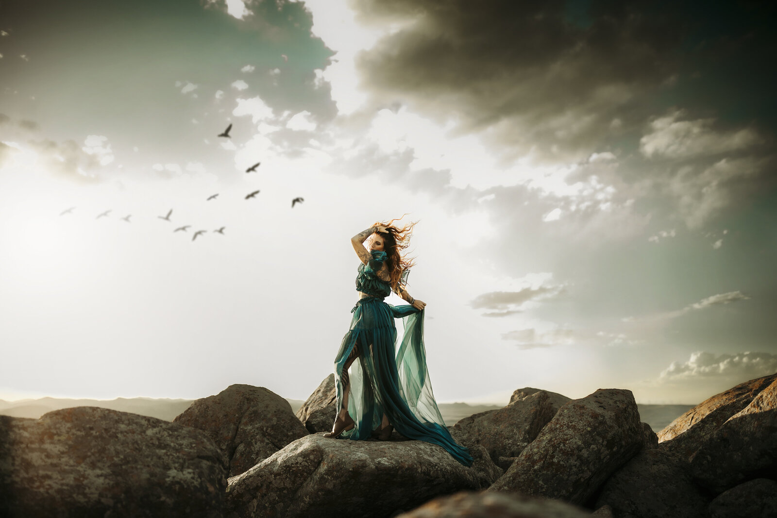 model poses on  mountaintop while birds fly over