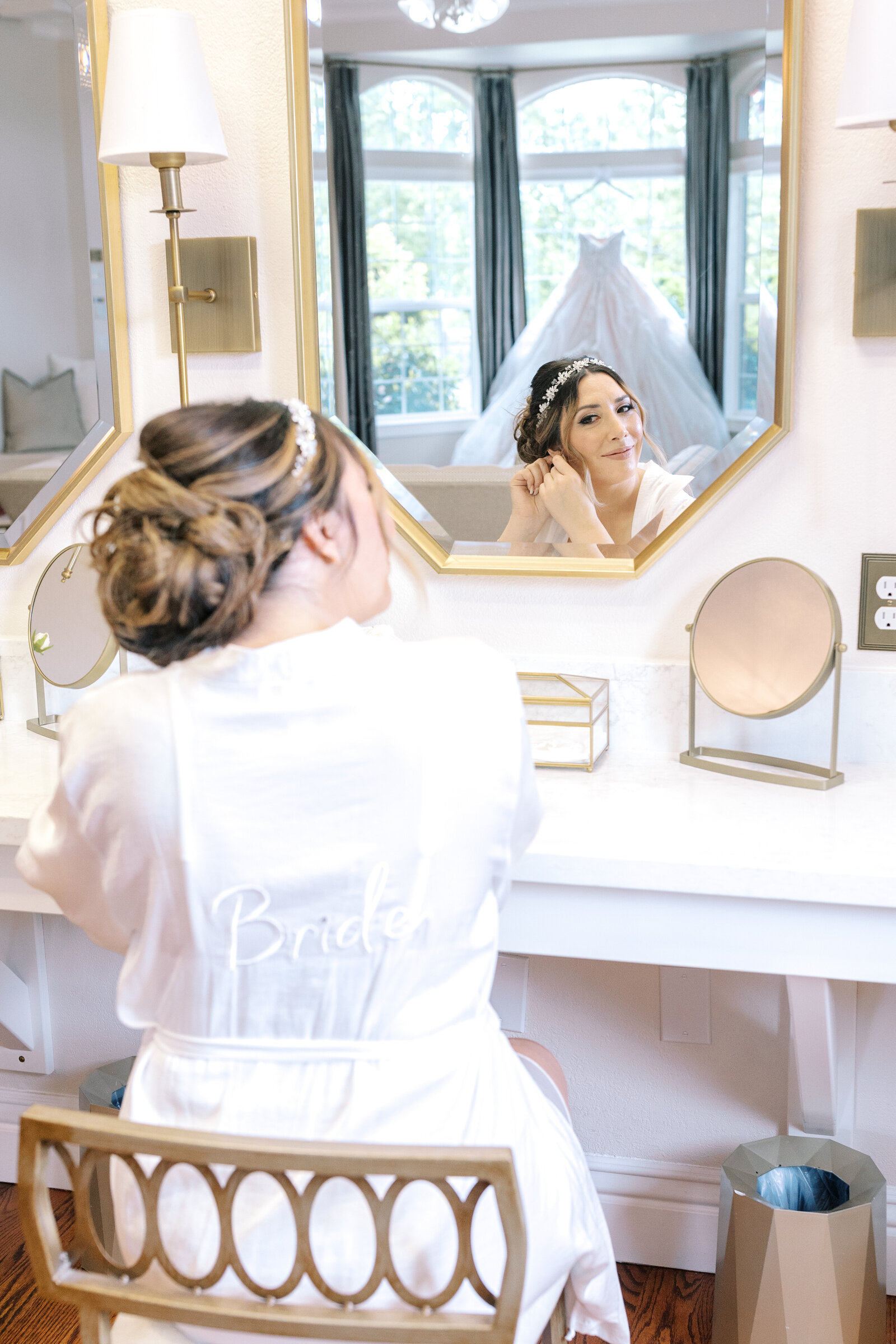 sacramento wedding photographer captures bride sitting in front of a mirror while putting on earrings with her wedding dress reflecting in the mirror