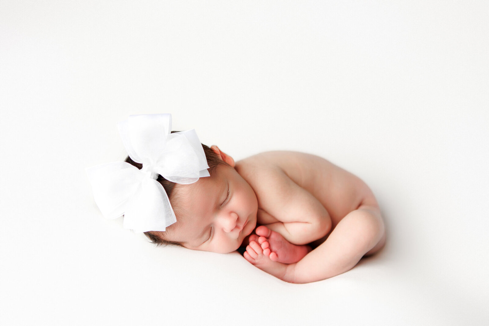 newborn baby girl ohot, womb pose, all white backdrop, baby wearing white bow, fresno, clovis, photographer