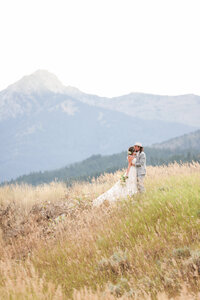 Couple kissing in a field of tall grass with mountain views in the background