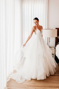 Bride twirling in an A-Line Tulle Princess Wedding Dress with spaghetti straps standing in front of white curtains