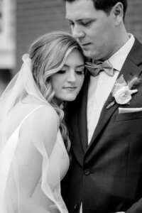Black and white photo of a bride with her head against the grooms shoulder as he is looking down at her
