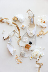 Flatlay wedding details image by Lifelong Photogaphy Studio featuring Jimmy Choo white pearl sandles, ring boxes, and gold details along with YSL perfume