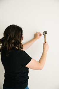 fallback shared on Invalid Date | A woman uses a hammer to put a nail in a white wall
