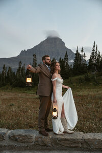 A bride and groom hold lanterns at dusk with a mountain peak behind them in Glacier National Park, captured by Sydney Breann Photography during their adventurous Montana elopement.