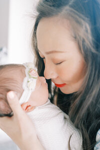 woman with dark hair gently touching her nose to her newborn baby's nose.