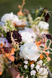 Close up photo of a Orange purple and white bouquet with greenery