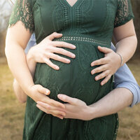 Two sets of arms wrapped around a pregnant belly in a green dress.