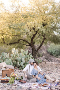 engaged couple sitting on blanket haaving picnic