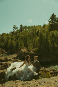 A man and woman hold hands while frolicking toward an old farm while the bride's dress and a united states flag flows in the wind