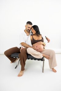 studio portrait of pregnant mother and her spouse smiling at eachother and embracing.