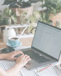 WOMAN TYPING ON A LAPTOP NEXT TO PLANTS AND CUP OF COFFEE