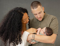 A couple holding their newborn baby with baby in dads arms and mom and dad looking down at baby girl.