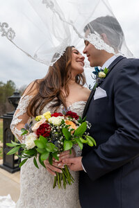 A newlywed couple about to kiss with a veil over their heads 