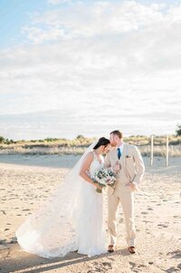 A wedding couple standing on a beach other as one kisses the other's head