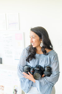 Photographer smiles while holding camera and lenses during Baltimore Maryland Brand Session photographed by Cait Kramer