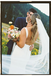 Bride and groom sharing a kiss in a wildflower meadow with mountain views, captured on film by a Washington wedding photographer.