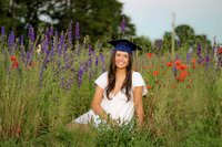 sitting in a monroe, NC flower field wearing a white dress and her graduation cap this charlotte senior is surrounded by red and blue wildflowers