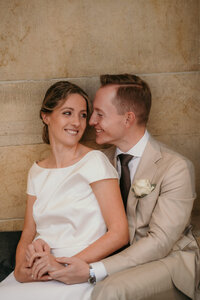 Bride and groom sit in a close embrace smiling at each other.
