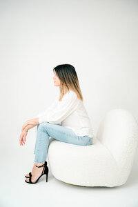Laura Mariani photographer, sitting in her white boucle chair in her Boulder CO studio.