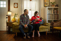 Two parents sitting on a couch while one holds a baby 