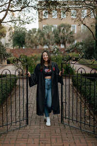 A senior female college student dressed in a USC shirt and their graduation gown poses for a portrait on the University of South Carolina Horseshoe.