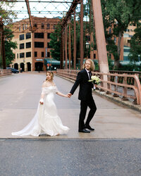 Minnesota bride  and groom in her elegant and modern wedding dress crosses the downtown street in Minneapolis holding hands as they look into the distance, captured by Toly Dzyuba Photography at Nicollet Island Inn.