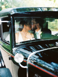 Image shot through a car window of a bride and groom kissing in the car