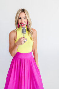 Renee Warren wearing lime green top and pink skirt holding podcast mic.