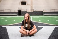 Vanderbilt senior in t-shirt sitting crisscross on football field