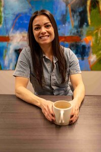 A woman sitting at a table, enjoying a cup of coffee in a cozy setting.
