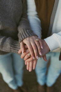 A couple stacking their hands together during a engagement session, with their rings prominently displayed, capturing a moment of love and commitment