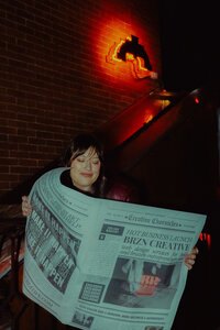 Gabi, founder of BRZN Creative, with brown hair and side swept bangs holding a large newspaper announcing the launch of the new web design business