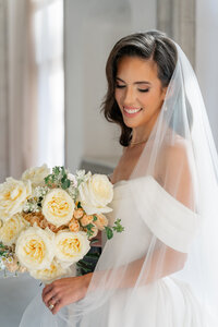A woman holding her bridal bouquet of yellow and peach florals