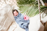 Newborn wrapped in blue swaddle with hibiscus flower after home birth in Oahu