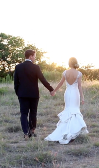 Groom and bride holding hands walking in field