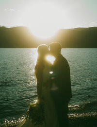 A bride and groom kissing at golden hour on the shore of a lake in Montana for their Glacier National Park elopement.